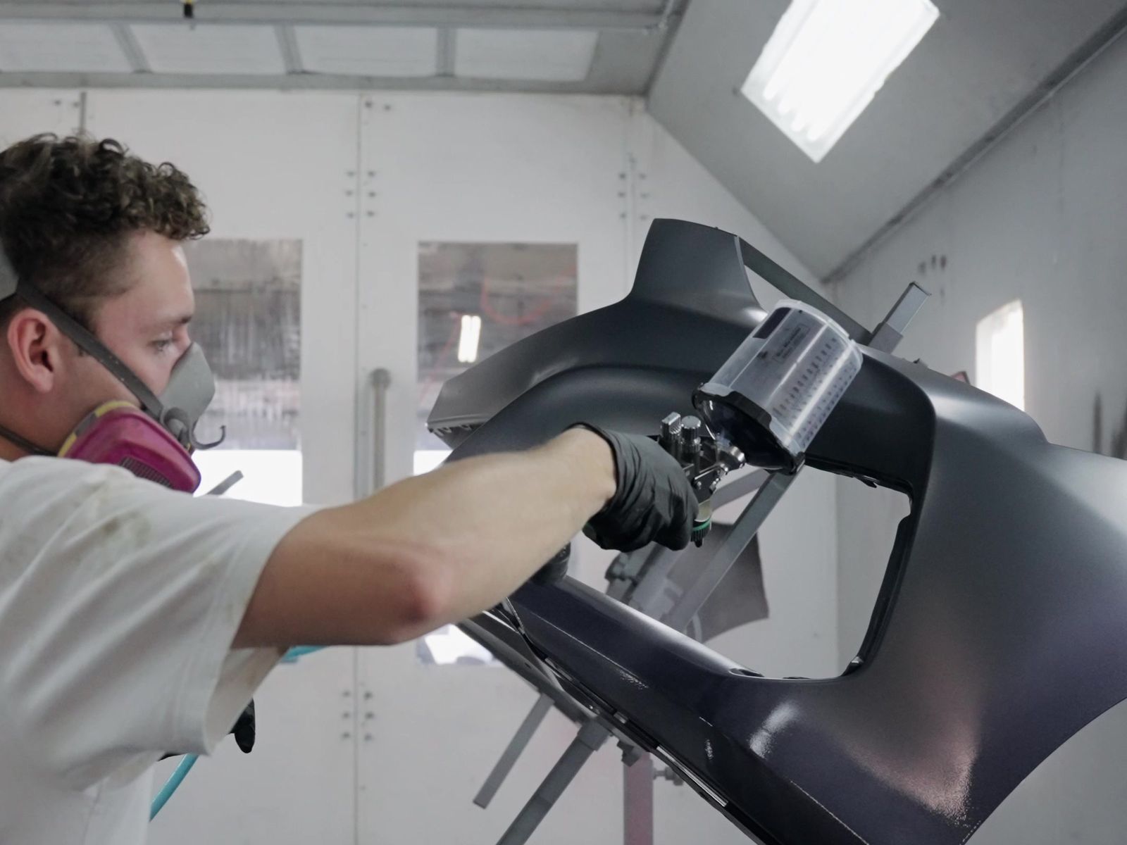 Painter applying paint to a bumper on a stand